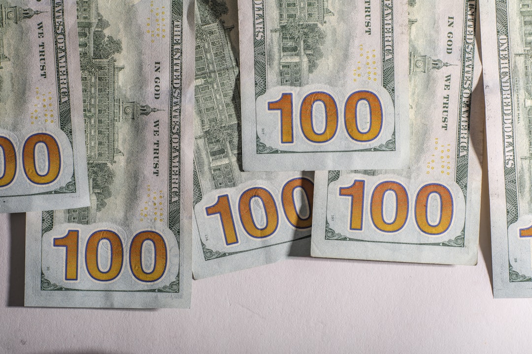 One hundred dollar bills scattered on a white surface.